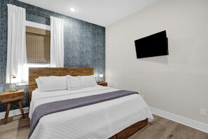 Habitación de hotel con cama, televisión montada en la pared y ventana con cortinas.