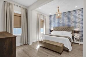 A bedroom with a large bed, a bench, a wooden dresser, and a patterned wall.