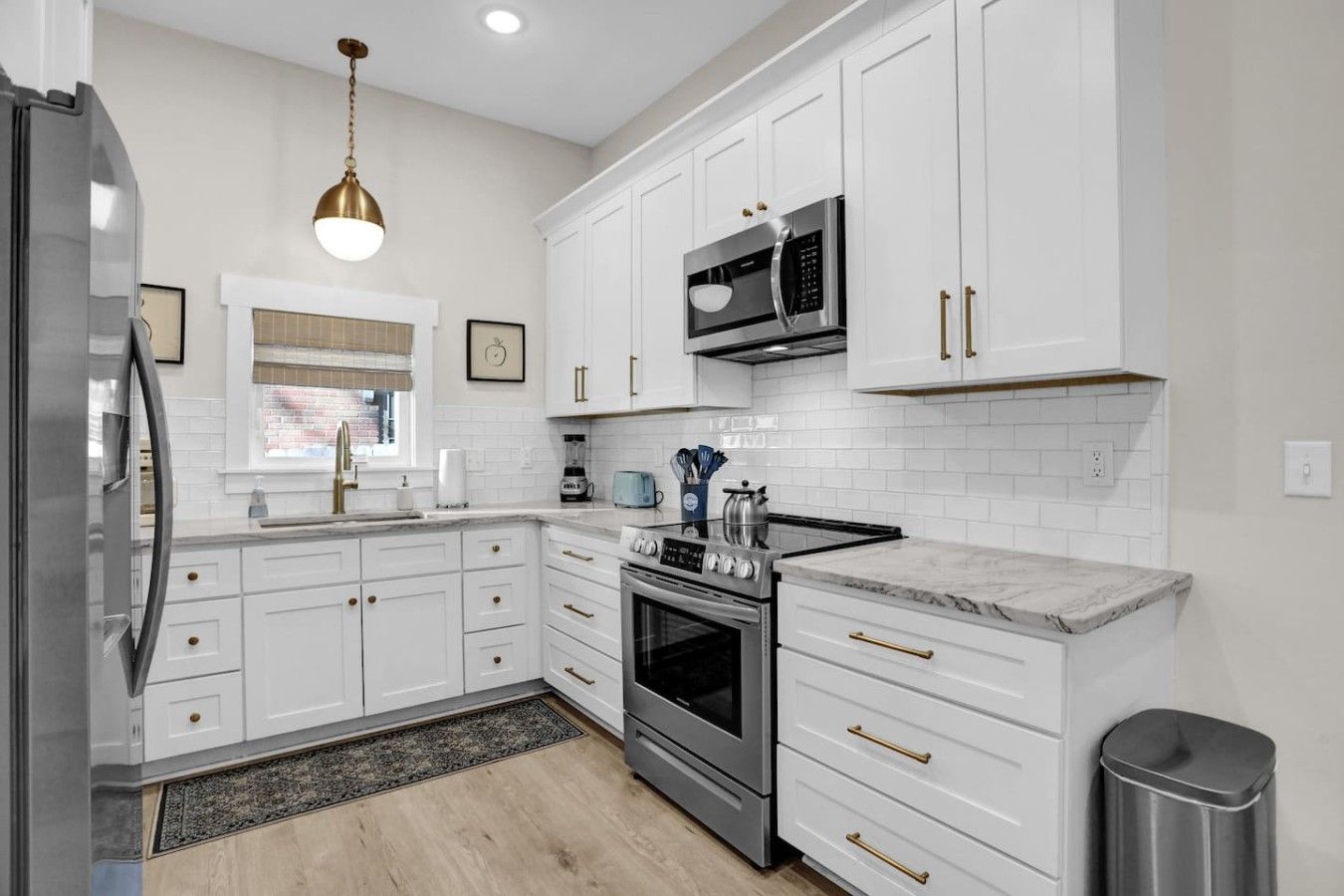 A modern kitchen with white cabinetry, stainless steel appliances, and a marble countertop.