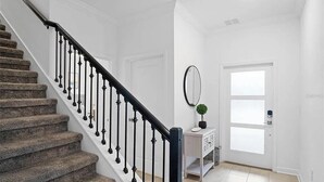 A staircase with a black railing, a white door, a small white console table with a mirror, and a potted plant. - Go!#34 - CHAMPIONS GATE (Davenport)
