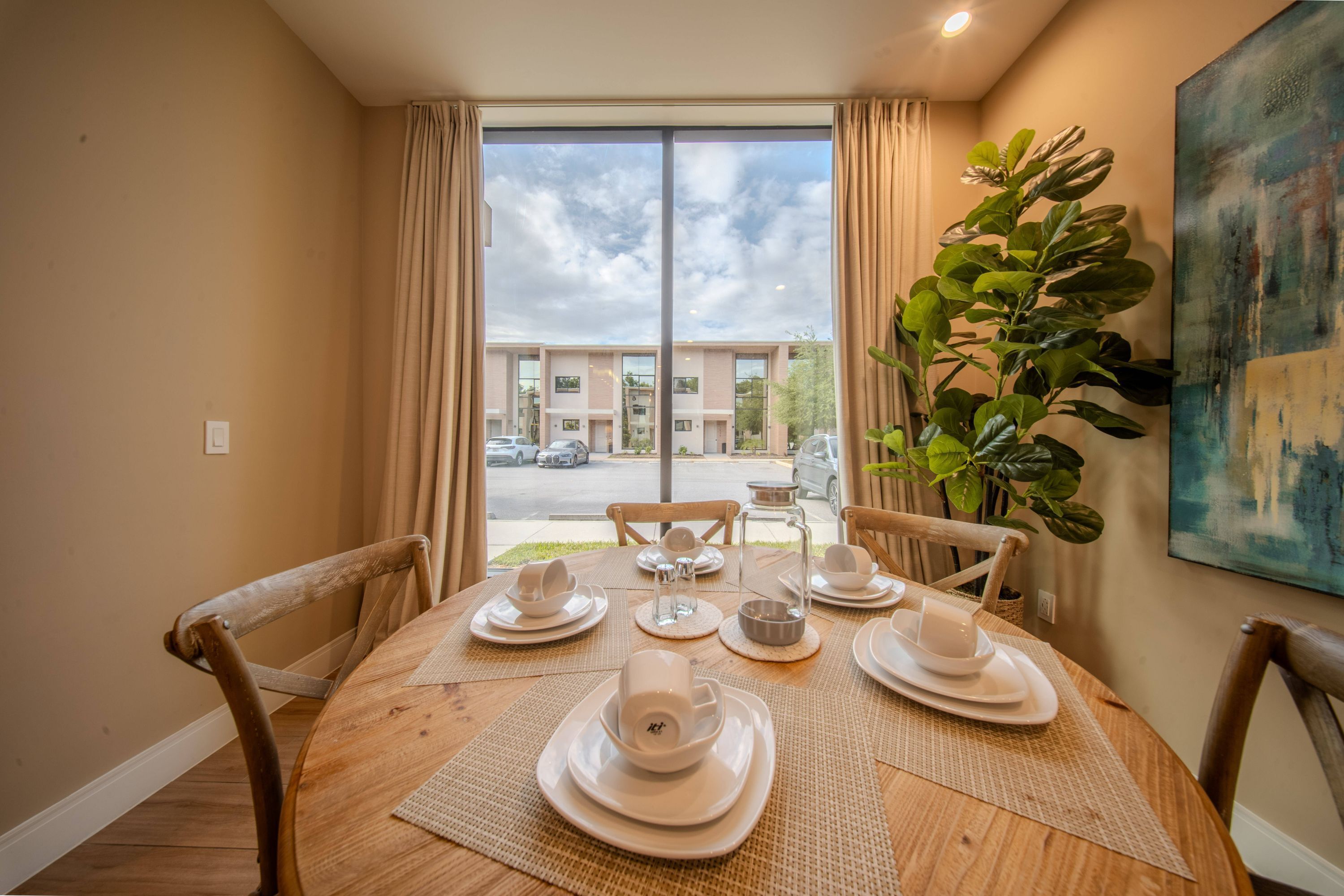 A dining table set with white dishes and a large plant in the corner.