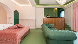 Un dormitorio con una cama, un banco tapizado en verde, un escritorio de madera y una televisión.