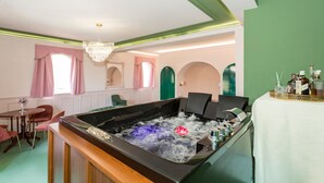 Una habitación con jacuzzi, candelabro, una mesa con botellas y pared verde.