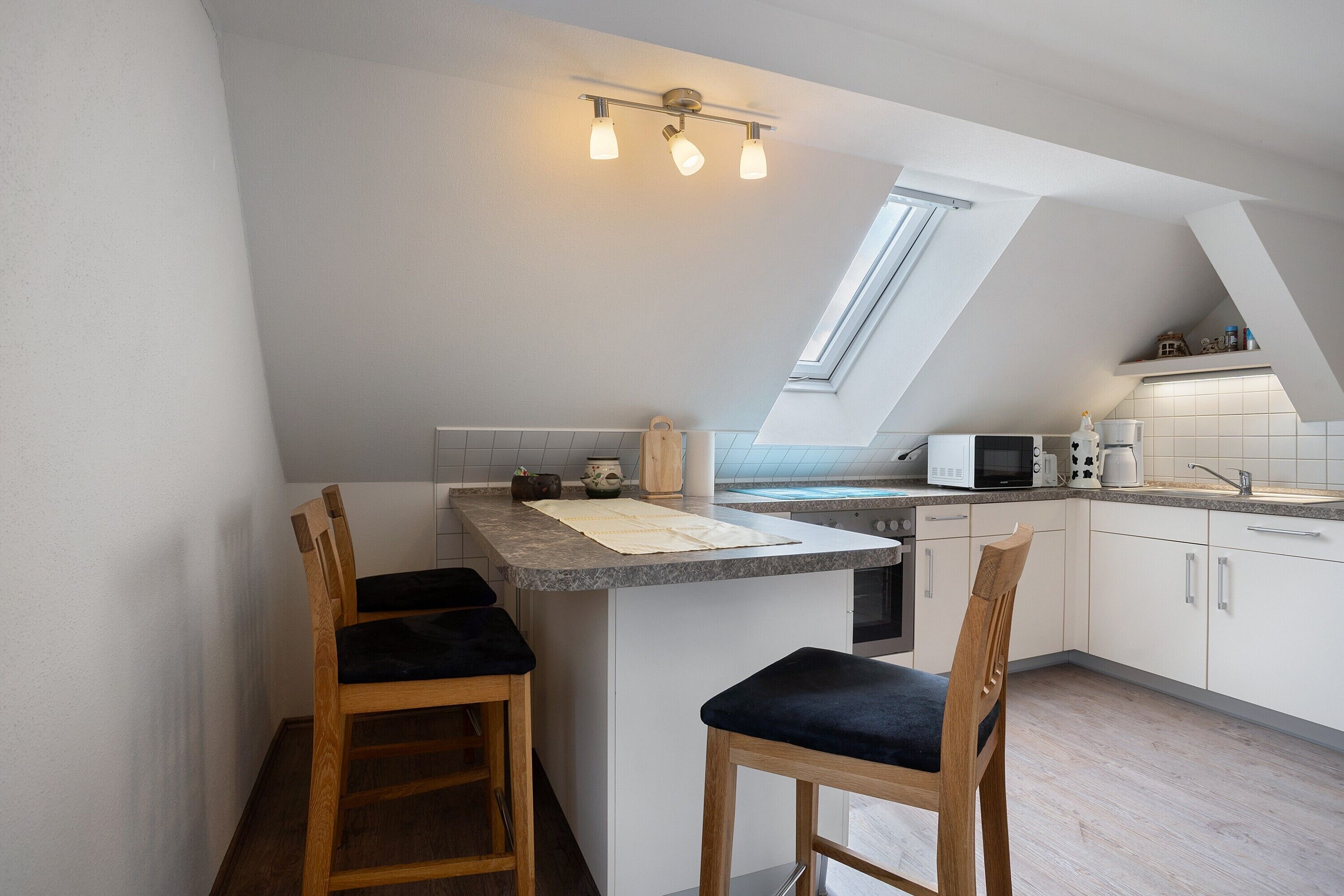 A kitchen with a skylight, a microwave, a kettle, and two bar stools.