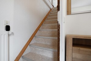A staircase with a wooden handrail, a white wall, and a white door.