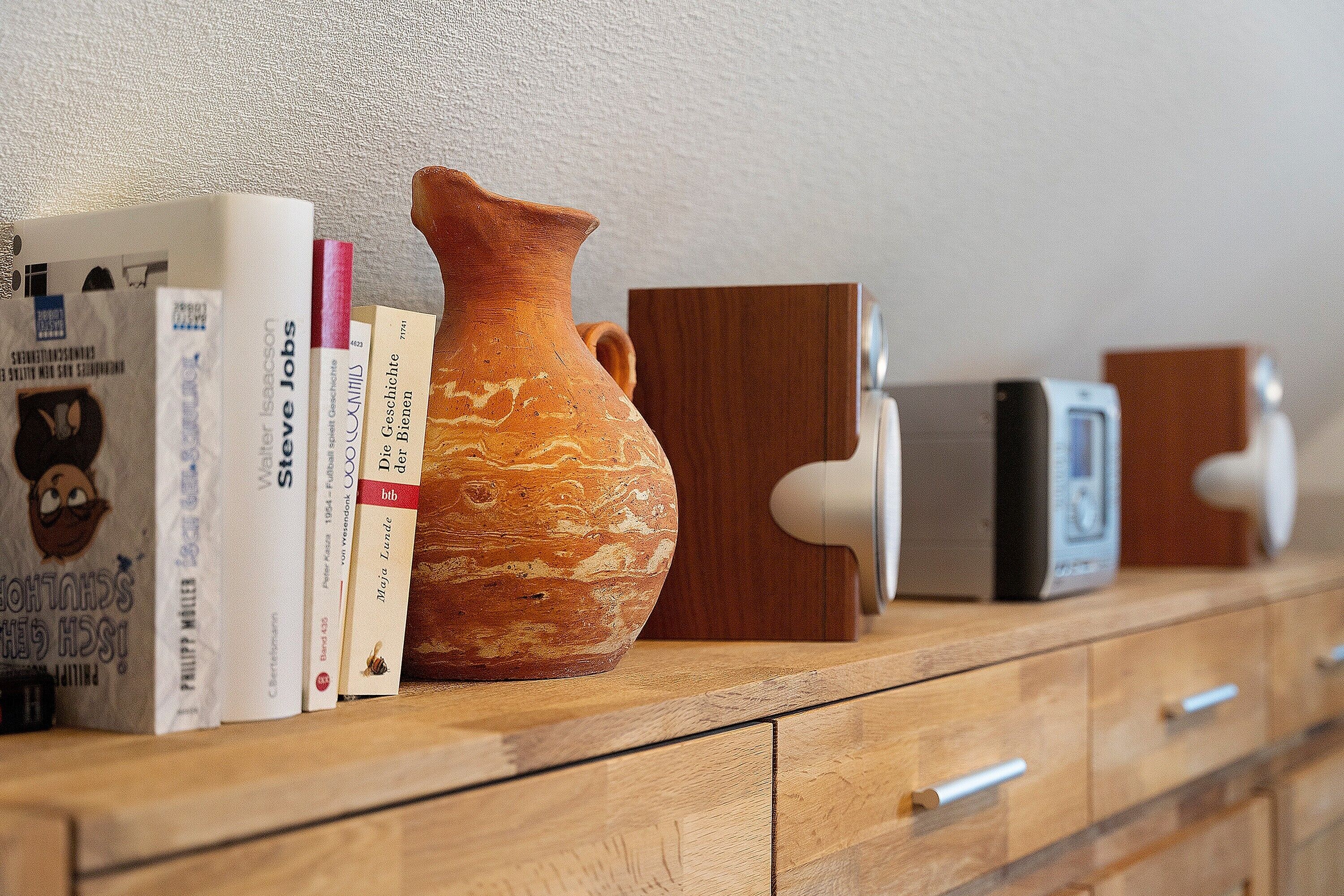 A wooden dresser with books, a ceramic vase, and electronic devices.