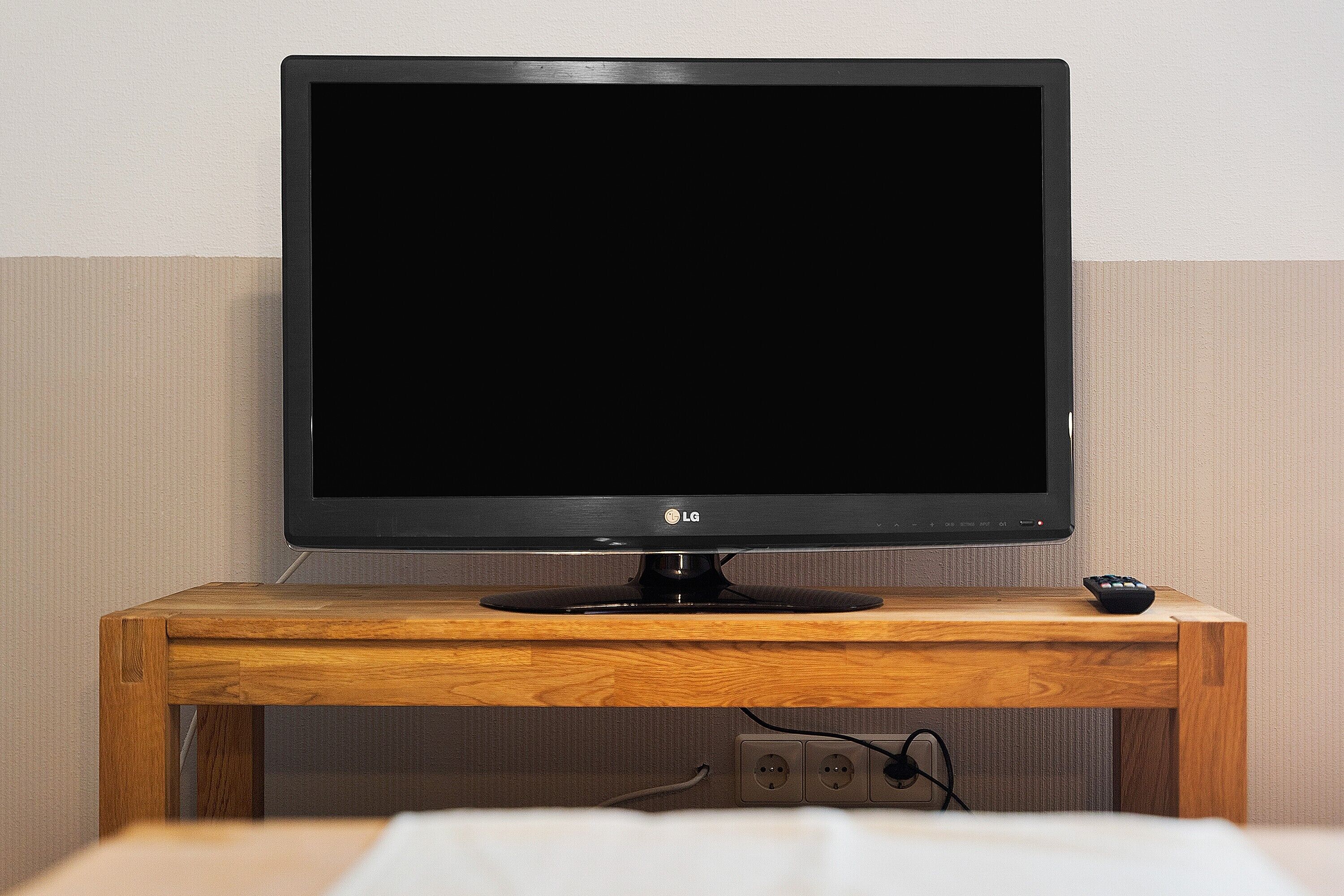 Ein Flachbildfernseher auf einem Holzständer, daneben eine Fernbedienung.