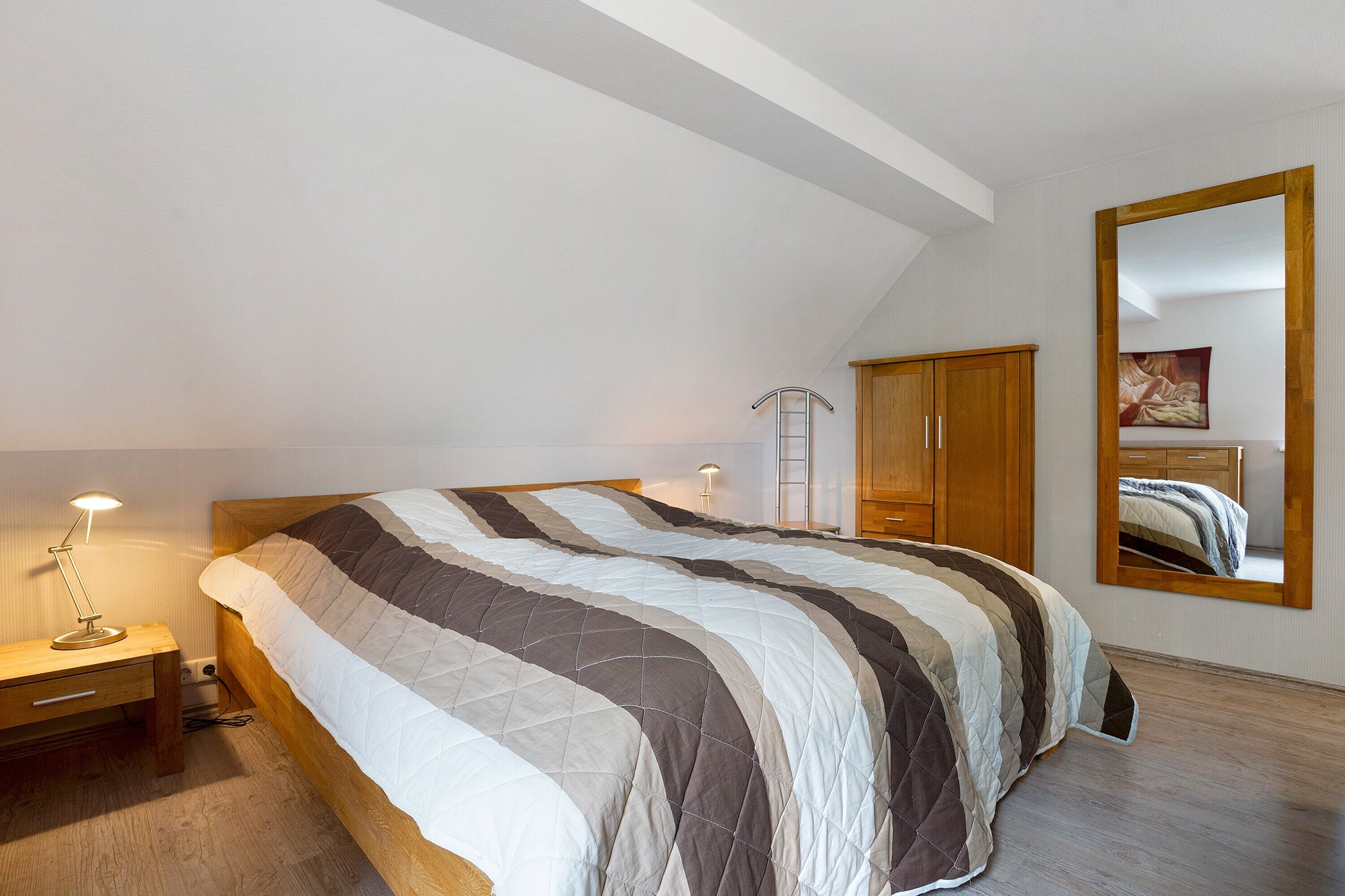 A bedroom with a bed, bedside table, lamp, wardrobe, and a large mirror.