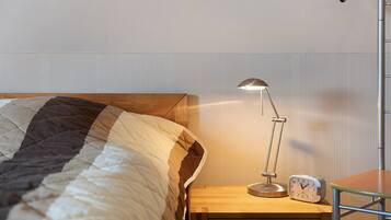 A neatly made bed with a striped blanket, a bedside table with a lamp and an alarm clock, and a chair.