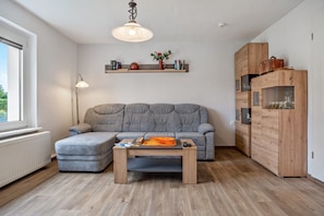 A living room with a grey sofa, a wooden coffee table, a wooden cabinet, and a pendant light.