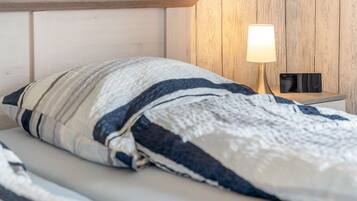 Ein Bett mit gestreiftem Kopfkissen und einer Decke, eine Nachttischlampe und ein kleines schwarzes Objekt auf dem Nachttisch.