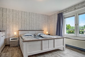 Ein Schlafzimmer mit einem hölzernen Bett, Nachttischen, einem Fenster mit Blick und einer Heizung.