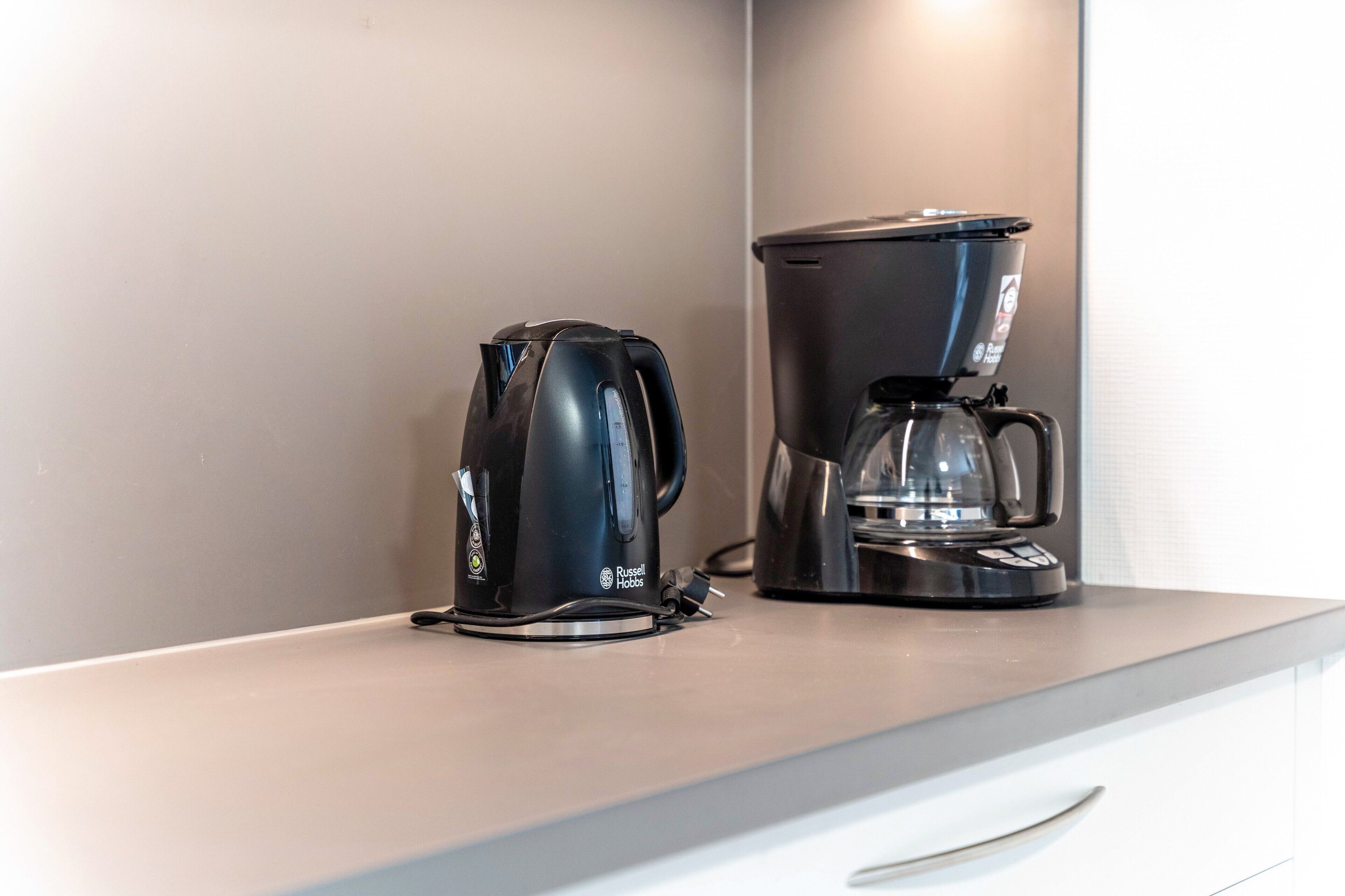Eine Küchenarbeitsplatte mit einem schwarzen Wasserkocher und einer schwarzen Kaffeemaschine.