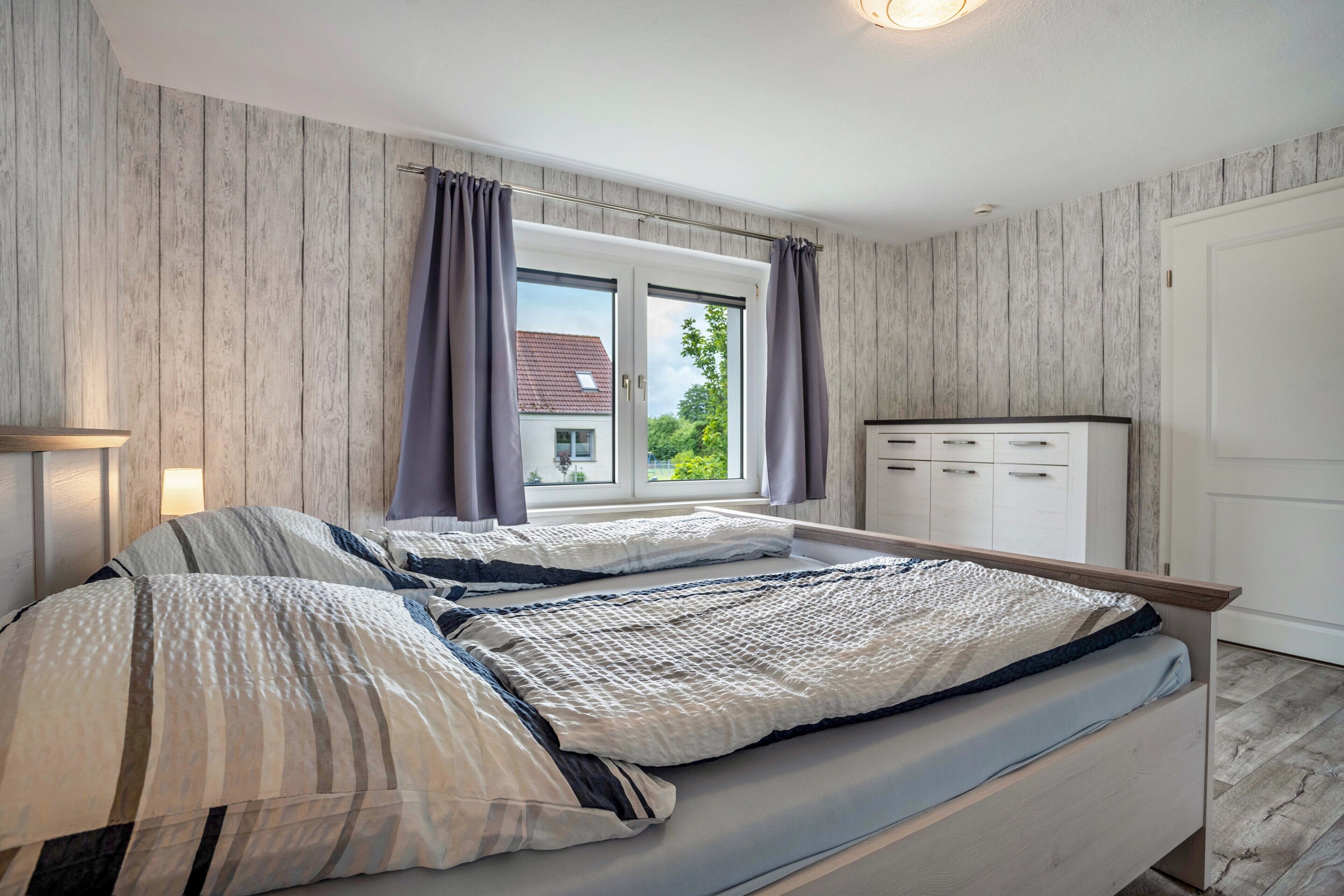 Un dormitorio con cama, ventana con cortinas, mesita de noche y armario.