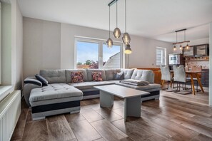 A modern living room with a sectional sofa, a dining table, and a kitchen area with a window. - Apartment '3' with Wi-Fi (Gribow)
