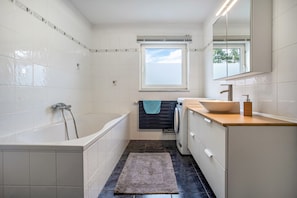 A modern bathroom with a bathtub, a sink, a mirror, and a window.