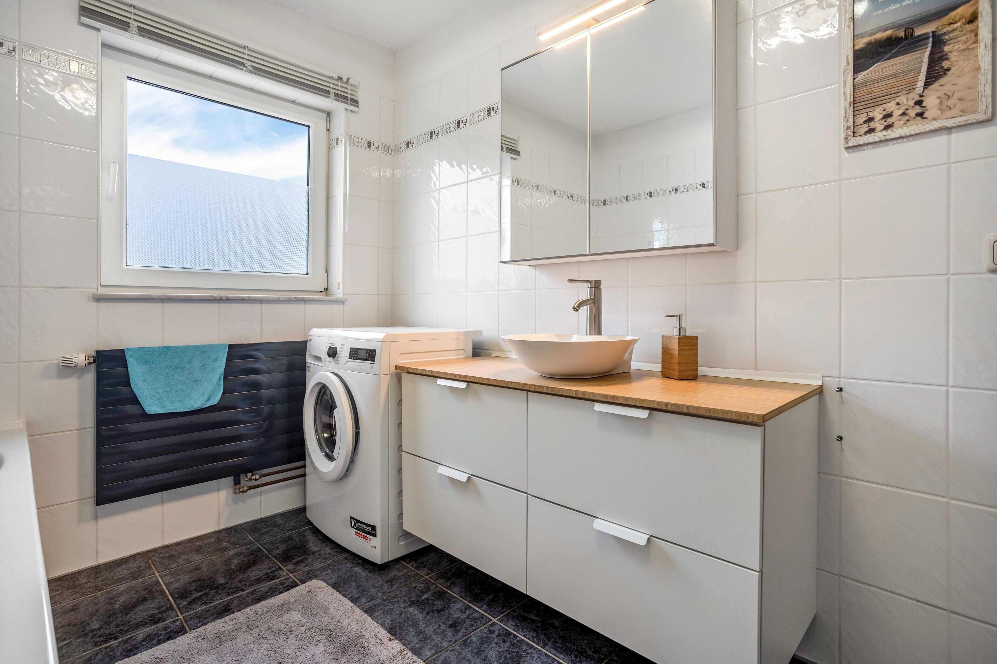 Un baño pequeño con lavadora, lavamanos con encimera de madera y un espejo grande.
