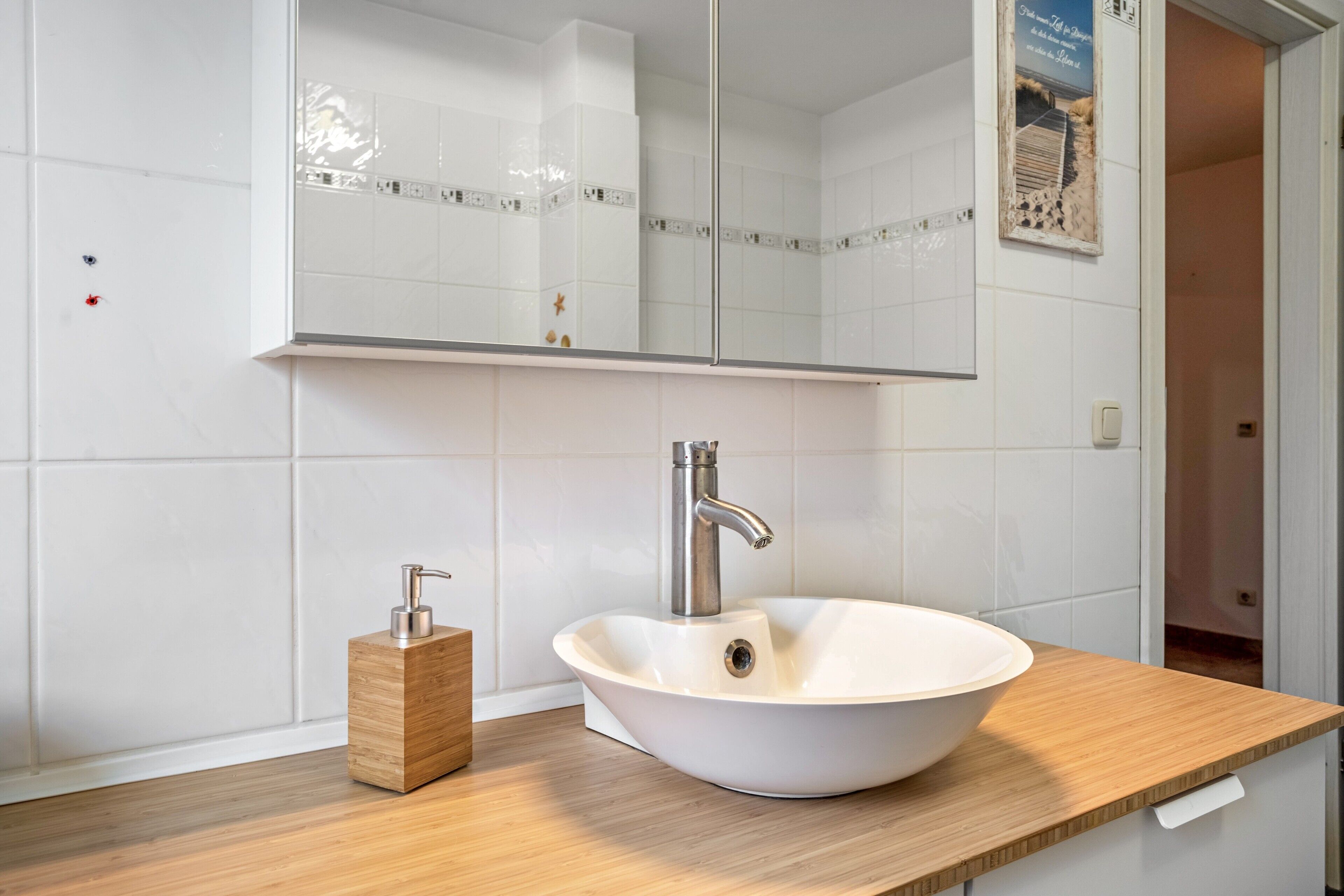 A bathroom with a white sink, a wooden soap dispenser, and a mirror above the sink.