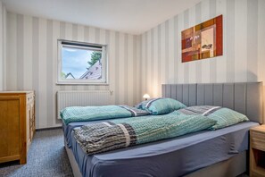Un dormitorio con cama, ventana, radiador, cómoda de madera y una obra de arte en la pared.