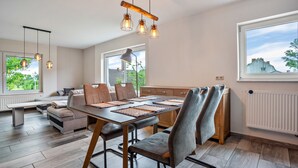 Un comedor moderno con una mesa de madera, sillas tapizadas en gris e iluminación colgante.