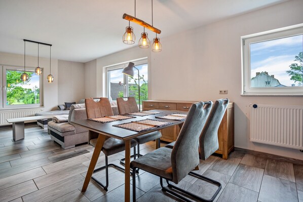 A modern dining area with a wooden table, grey upholstered chairs, and pendant lighting.