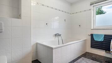 A bathroom with white tiles, a bathtub, a window, and a towel rack.