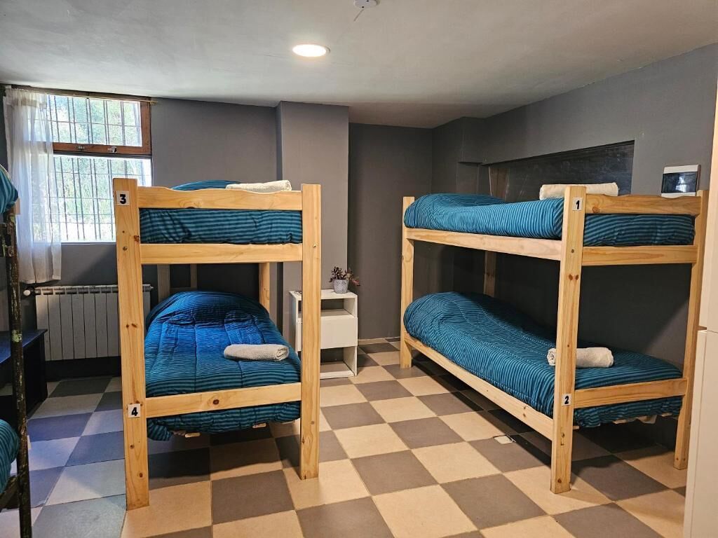 A dormitory room with bunk beds, a small table, and a window with curtains.
