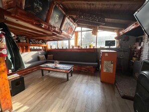 A cozy room with a wooden ceiling, a sofa, a coffee table, and a television. - Refugio Aku Hostel (San Carlos de Bariloche)