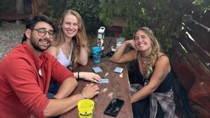 Trois personnes sont assises à une table en bois, à l'extérieur, avec de la verdure en arrière-plan.