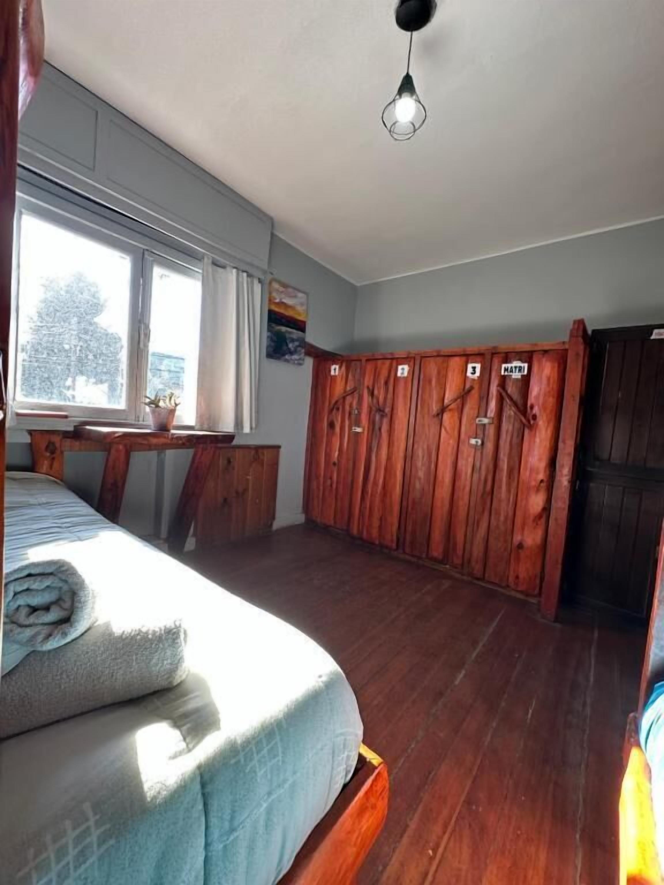 A room with a bed, wooden wardrobe, a window with curtains, and a hanging light fixture.
