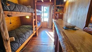 Un intérieur en bois avec des lits superposés, un comptoir en bois et une vue sur l’extérieur, visible à travers une porte.