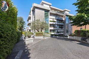 A modern multi-story building with balconies, a paved entrance, and surrounding greenery. - Suite House Cassia: Vacation Home with Mountain View, Wi-Fi, and Air Conditioning (Roma)