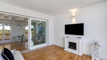Un salon moderne doté d’un téléviseur à écran plat fixé au-dessus d’une cheminée, d’une porte vitrée donnant sur un coin repas et d’un plancher en bois.