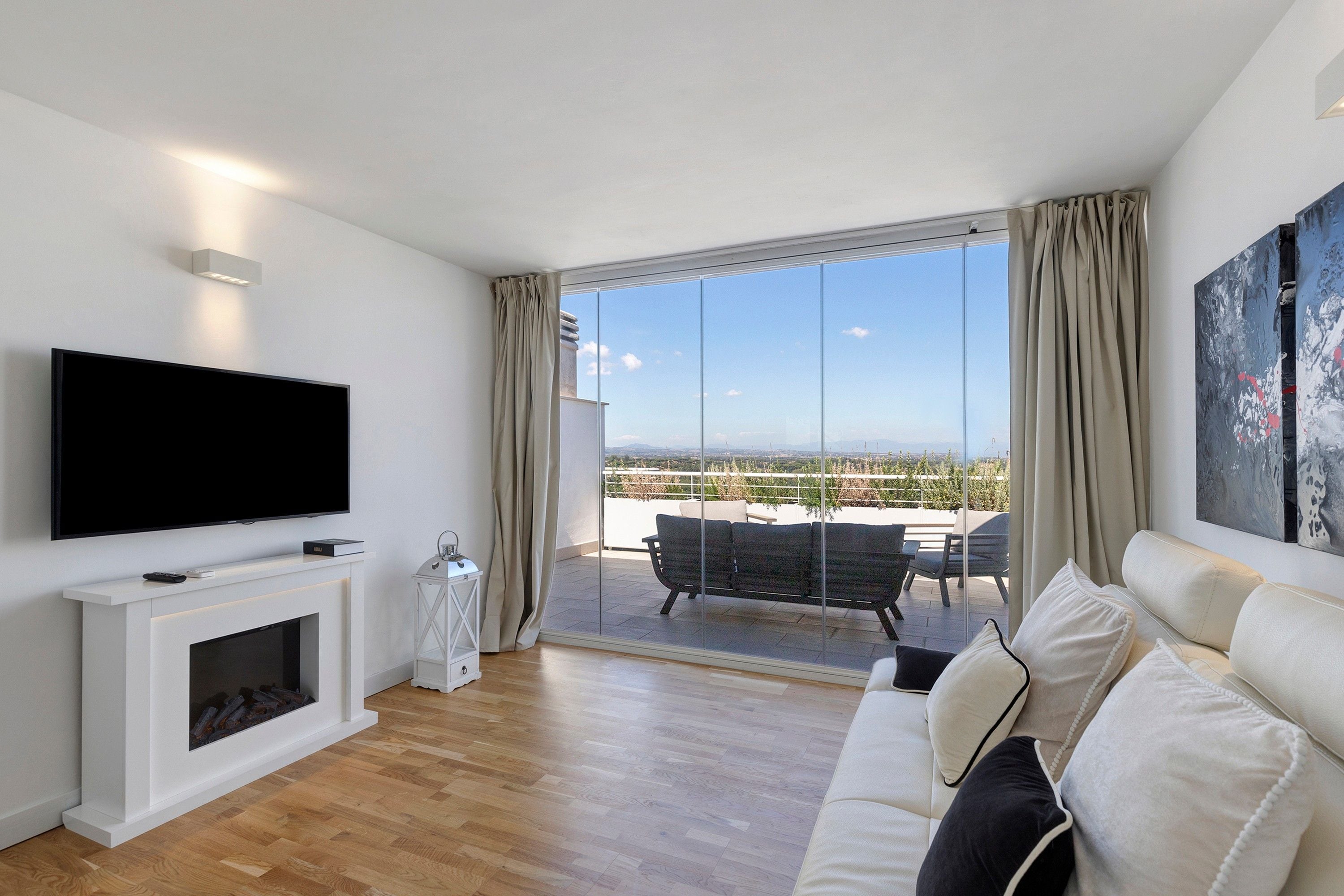 Ein modernes Wohnzimmer mit Flachbildfernseher, Kamin, einer Couch und einem Balkon mit Gartenmöbeln.