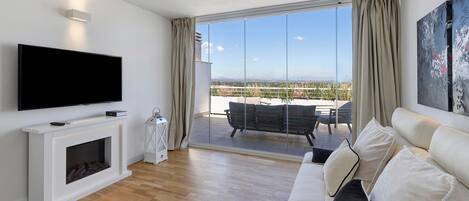 Ein modernes Wohnzimmer mit Flachbildfernseher, Kamin, einer Couch und einem Balkon mit Gartenmöbeln.