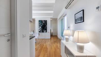 Un couloir moderne avec un plancher en bois, une console blanche agrémentée de lampes et un tableau encadré accroché au mur.
