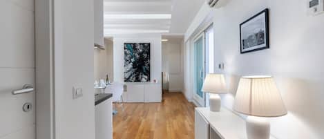 Ein moderner Flur mit Holzboden, einem weißen Konsolentisch mit Lampen und einem gerahmten Bild an der Wand.