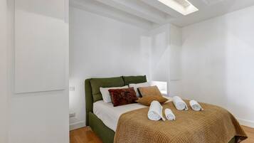 Un lit bien fait, avec une tête de lit verte, du linge de lit blanc et une couverture marron. On peut voir des serviettes enroulées sur le lit et une couverture marron à texture intéressante.
