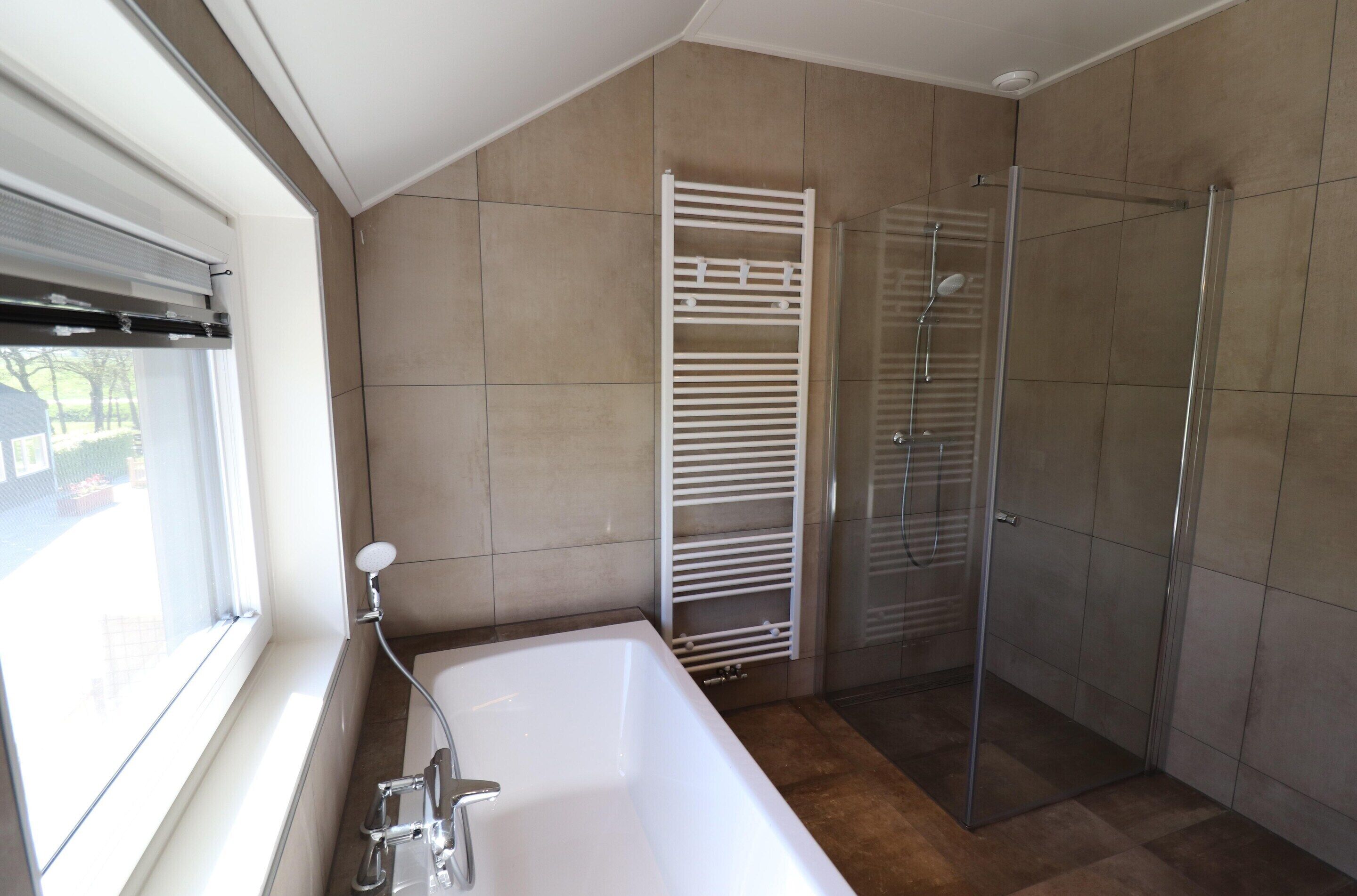 A bathroom with a bathtub, a glass shower enclosure, and a window.