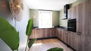 A modern kitchen with wooden cabinets, a built-in oven, and a large window. - Newly Built Group Villa in Friesland (Leons)