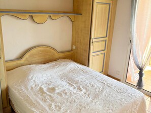 A bed with a wooden headboard, a wardrobe with a blue trim, and a window with a curtain. - Apartment for 8 by the Beach (Capbreton)