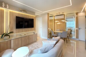 A modern living room with a flat-screen TV, a sofa, a dining area with chairs, and a kitchen with wooden cabinets. - View Butantã by Wecare Hosting (São Paulo)