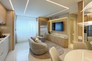 A modern living room with a sofa, a dining table, and a kitchen area with a TV. - View Butantã by Wecare Hosting (São Paulo)