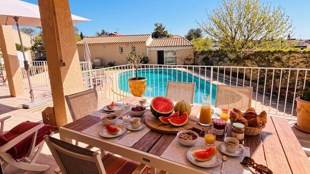 Mesa de jantar com itens de café da manhã, piscina e vista para casas.