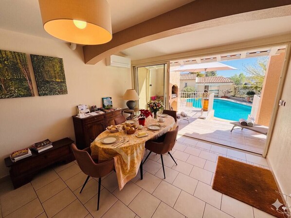 A dining area with a table set for two, a lamp, and a view of a swimming pool.