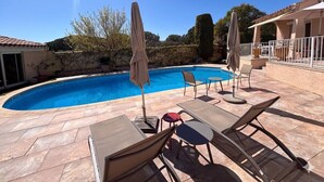 Uma piscina com espreguiçadeiras e guarda-sóis, ladeada por um pátio de pedra.