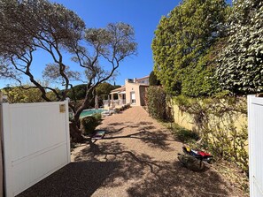 A pathway leading to a building with a pool, surrounded by trees and a white gate.