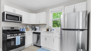 A modern kitchen with white cabinets, stainless steel appliances, and a window with a view of trees. - Elegant 1 Bed Steps to Metra & Dining in Lake Forest! (Lake Forest)