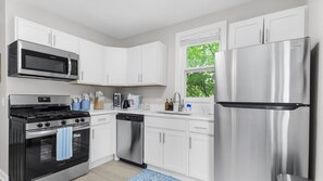 Une cuisine moderne avec des meubles blancs, des appareils en acier inoxydable et une fenêtre donnant sur les arbres.