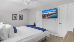 A hotel room with a bed, a ceiling fan, a cityscape painting, and two framed pictures on the wall. - Elegant 1 Bed Steps to Metra & Dining in Lake Forest! (Lake Forest)
